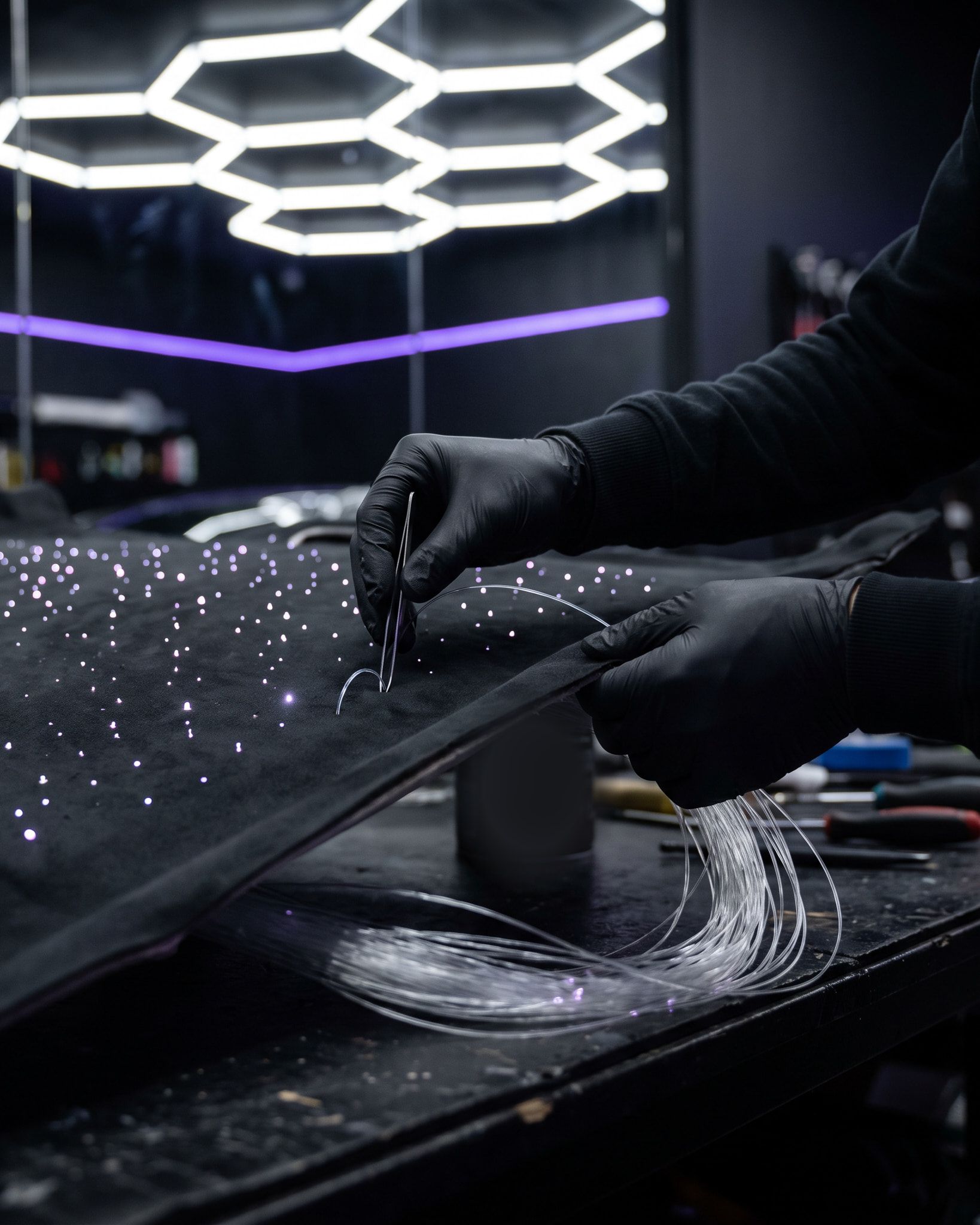 Behandschuhte Hände setzen mit einer Pinzette Lichtfasern einzeln in einen ausgebauten schwarzen Dachhimmel