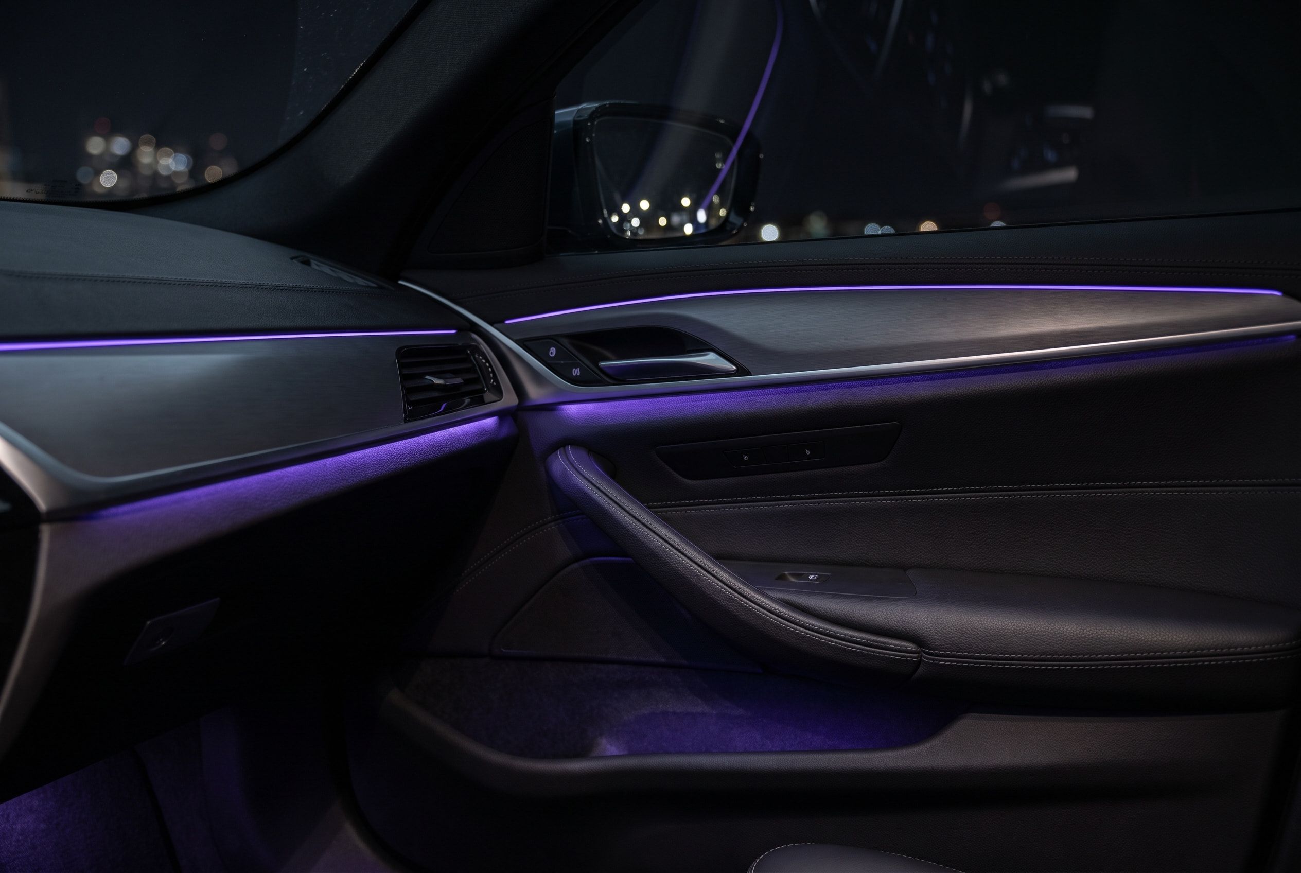 Fahrzeuginnenraum bei Nacht mit violetter Ambientebeleuchtung in Türen und Armaturenbrett
